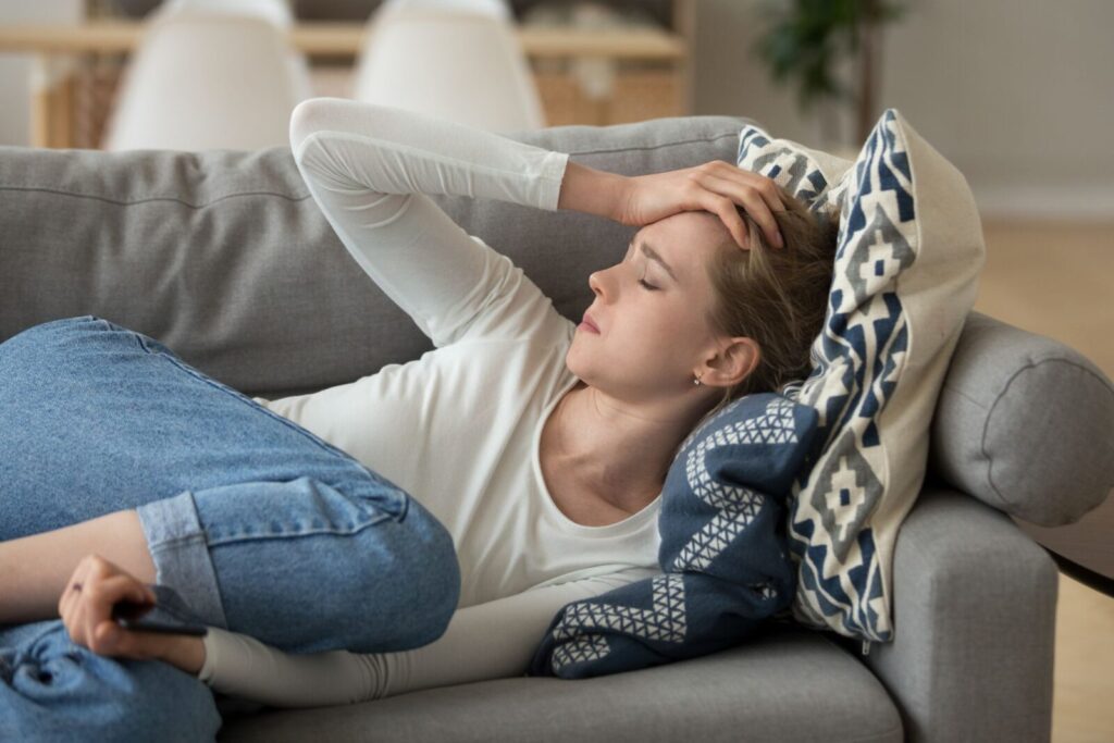 Young woman laying on a cough with her hand on her head experiencing mental health concerns. 