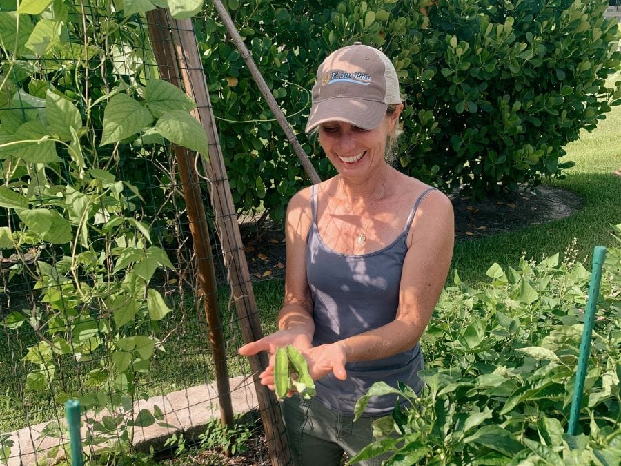 Farm Stand's gardener, Heidi Hoover, standing in the garden holding winged beans.