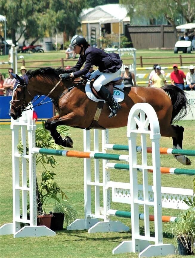 A man jumping a performance horse at a show.