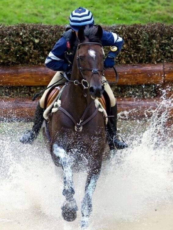 Someone riding an eventing performance horse through a water jump.