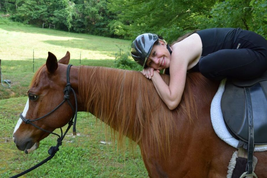 Cathy Woods performing a hip flexor yoga pose seated on a horse and leaning onto the horse's wither.